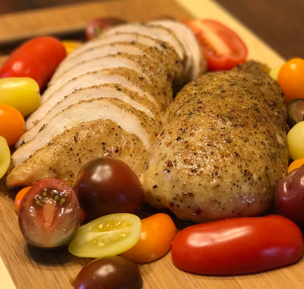 Cooked Turkey Breast partially sliced on cutting board with random sized tomatoes