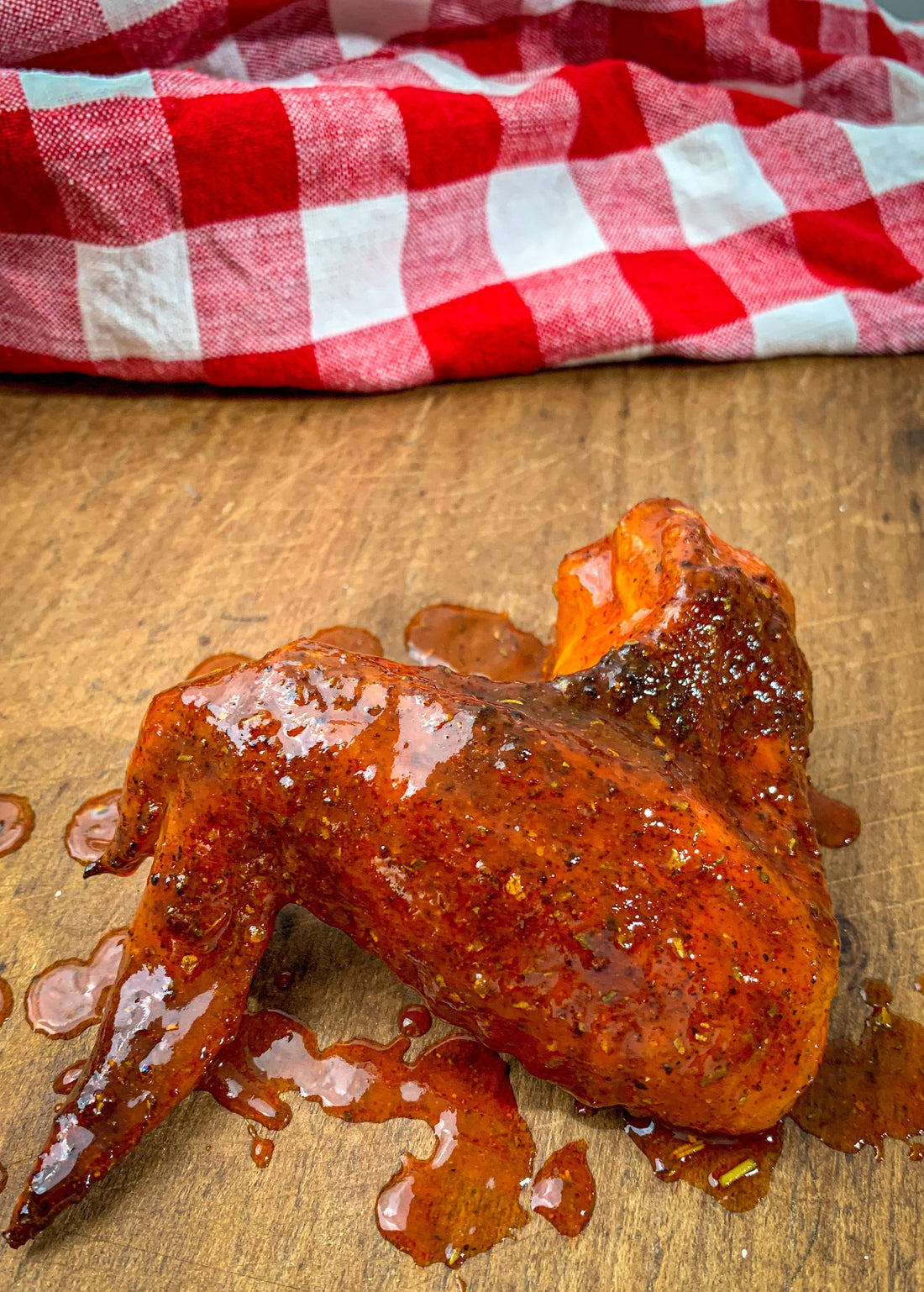 One smoked and sauced chicken wing on a rustic table with red and white table cloth.