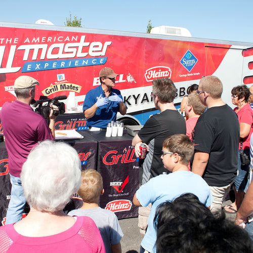 Event with people gathered around a food truck branded with 'American Grill Master' and 'Heinz'.